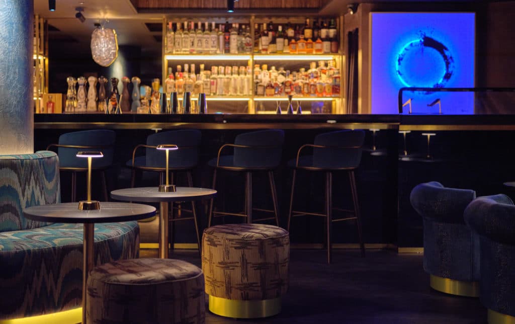 some of the seating area in front of the backlit bar at viajante87, with a large blue piece of lit decor to the right