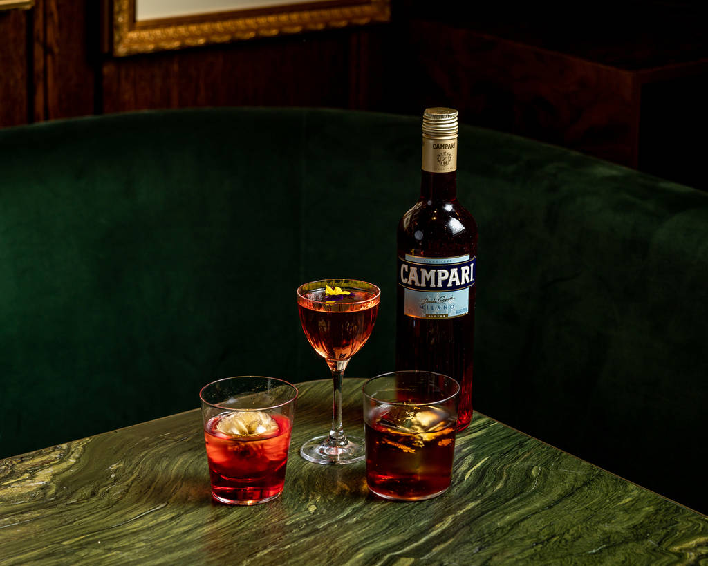 a trio of negroni's presented in different glasses next to a bottle of campari