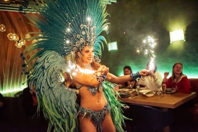 A woman in carnival style headress and outfit dances with sparklers