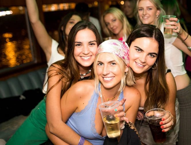 A group of women posing for photos with drinks aboard a boat party in London