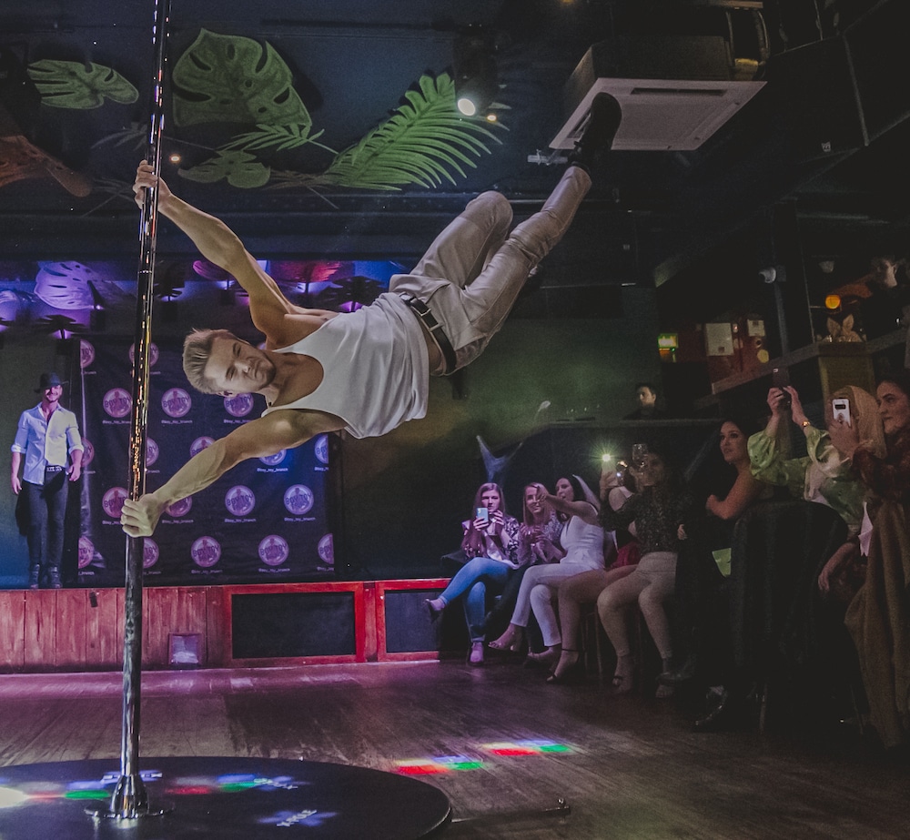 A man swinging around a pole at one of the best bottomless brunches in London