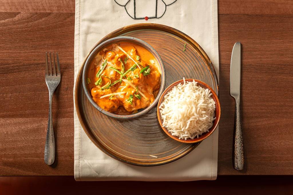 a plate with two bowls, one containing butter chicken and one containing rice