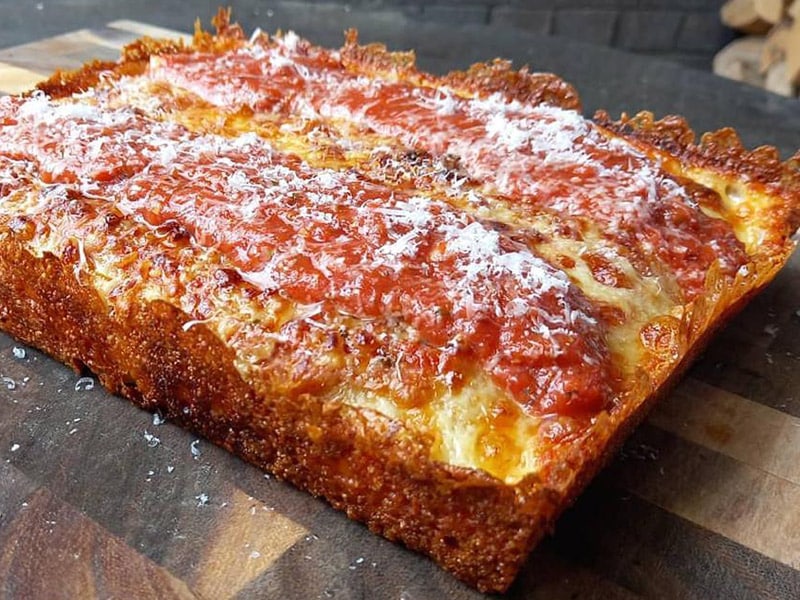 a thick Detroit-style pizza with crispy cheesy side and plenty of sauce on top