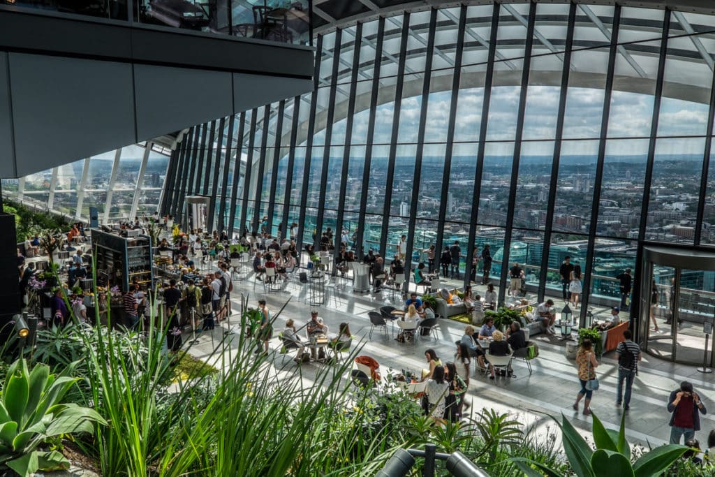 people sitting and standing around in front of the impressive skyline views from the sky garden