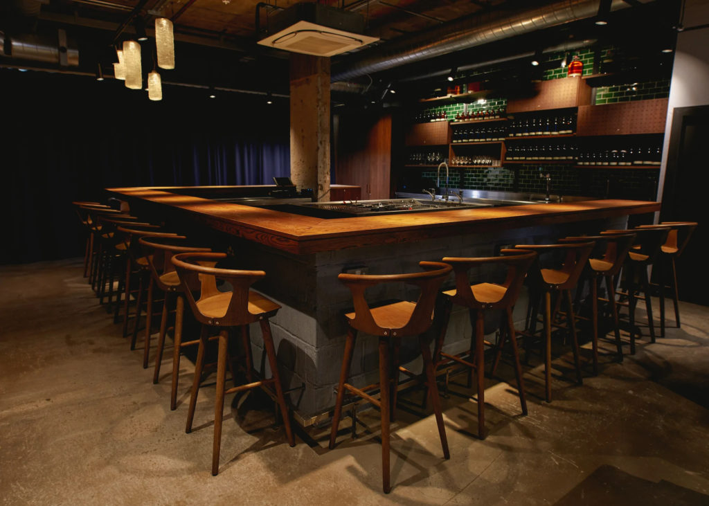 a horseshoe shaped bar surrounded by wooden stools in low lighting