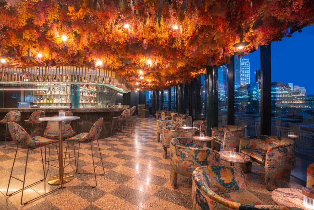 a shot of florattica, whose floral installation hangs above the bar and spread out seating area, with a view of london visible out the windows to the right