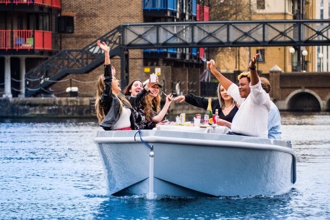 A group of friends wave from a GoBoat on a voyage around Canary Wharf.