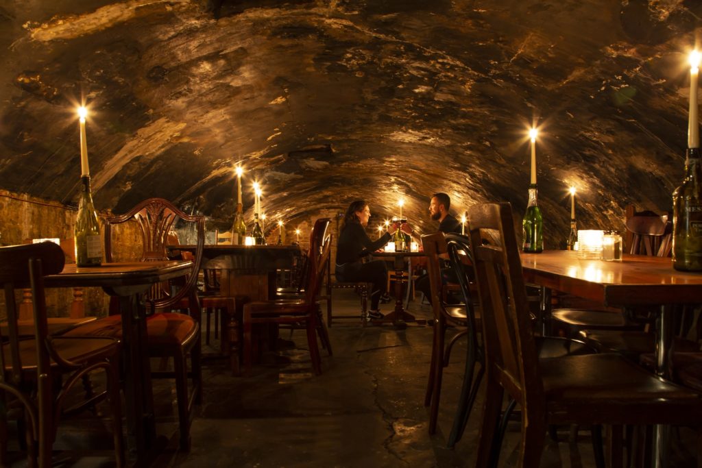 two people sat in the wine cave at Gordon's Wine Bar, clinking glasses in the low-ceilinged candle-lit atmosphere