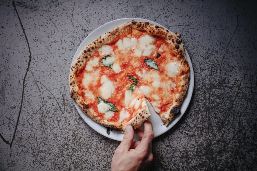 a hand grabbing a slice from a margherita pizza