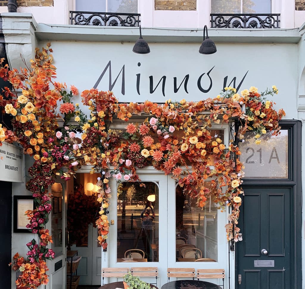 the frontage of minnow, one of london's prettiest restaurants, with blue paint, and autumnal flowers strung across the entrance