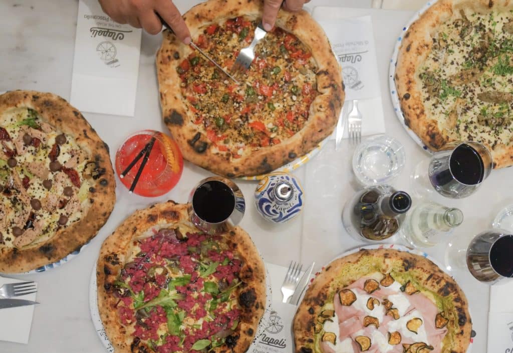 a selection of pizzas seen from above, with someone cutting into one of the pizzas