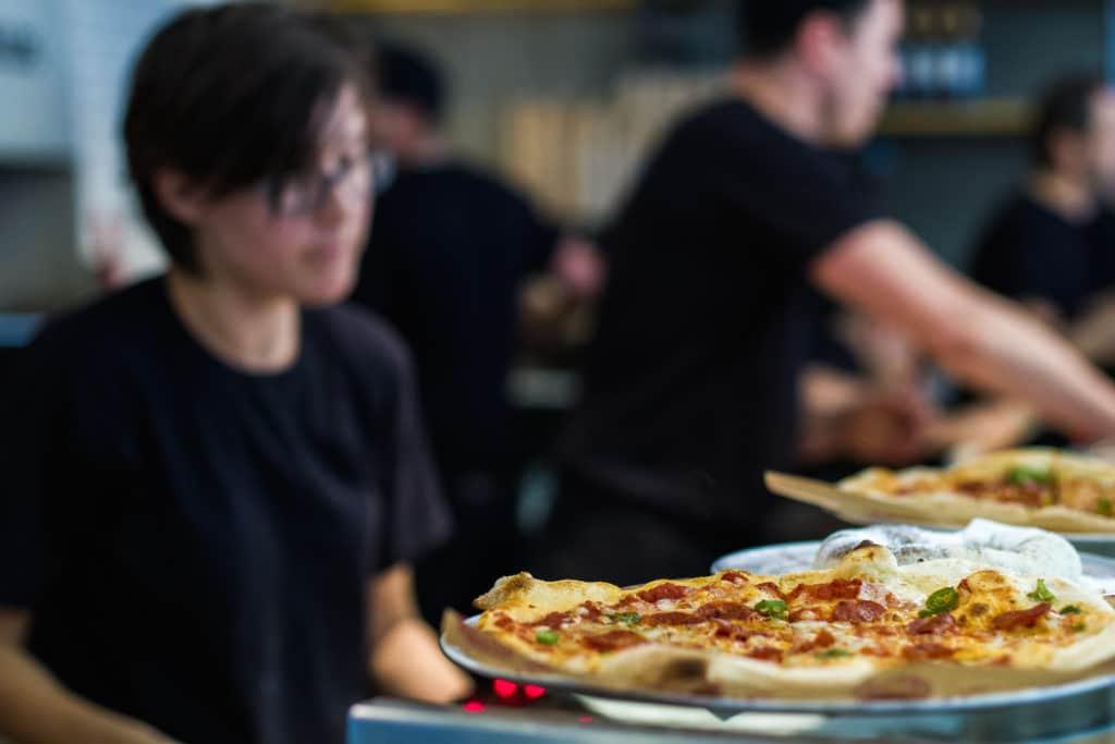 a pizza perched on a counter, with workers out of focus in the background