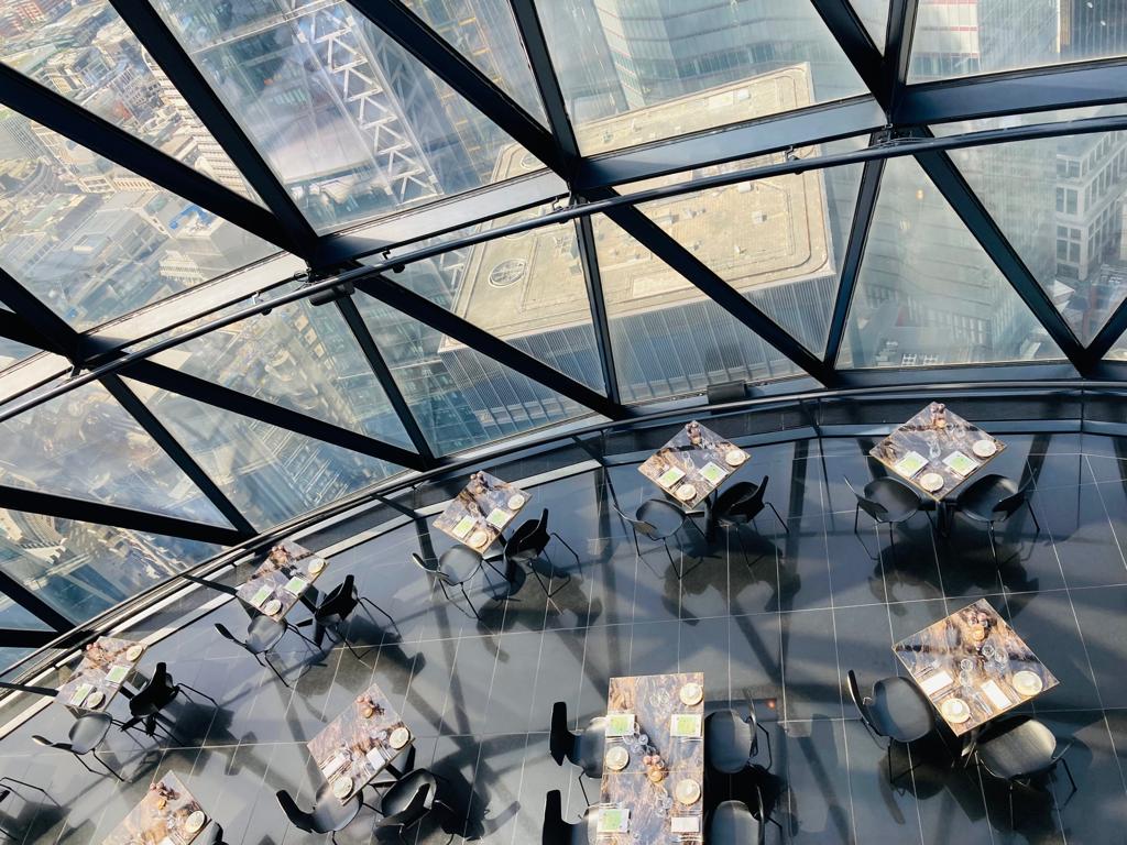 a top down shot of tables clustered around the searcys at the gherkin restaurant, with the view out of the gherkin visible