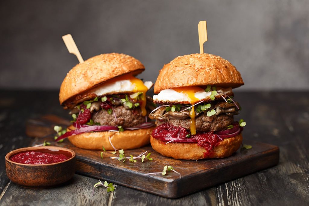 Two drool-worthy burgers being served with burger sauce, mayonnaise and more