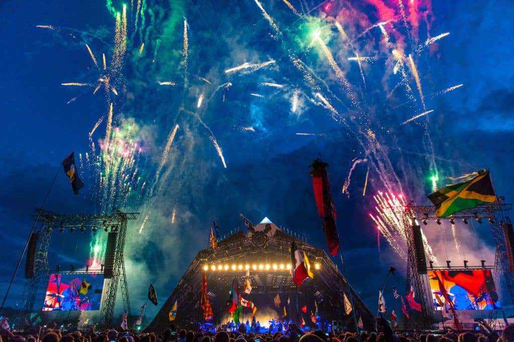 fireworks and flags fill the sky in front of the Glastonbury festival stage in the early evening