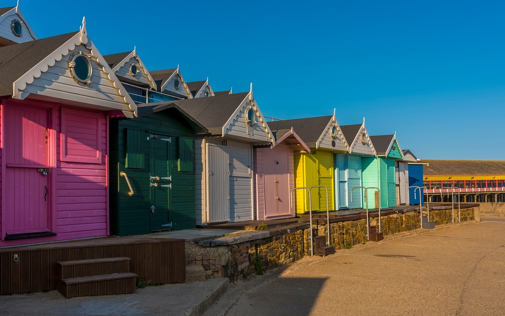 An early evening view of the beach huts along the promenade towards the pier at Walton on the Naze, UK in the summertime