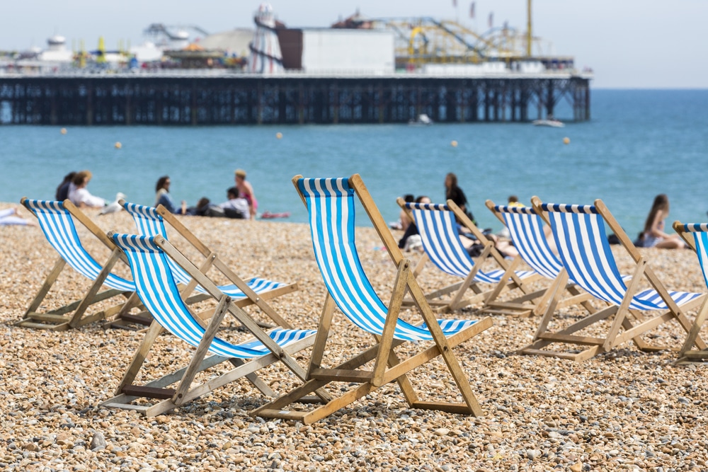 Traditional old-fashioned blue and white striped deckchairs on the beach in front of the Palace Pier, Brighton, East Sussex, UK