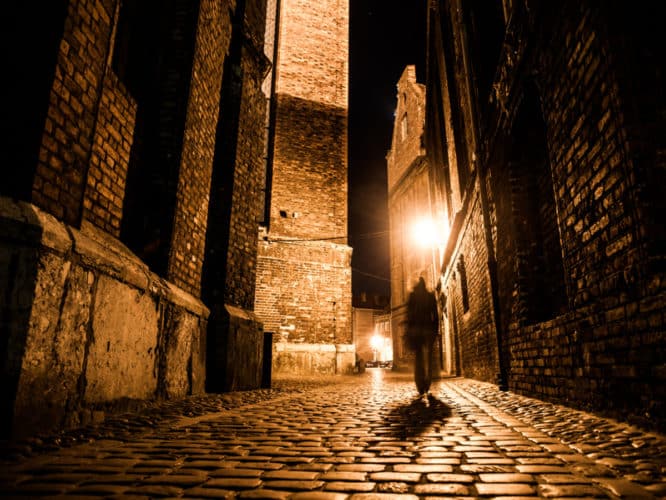 The shadowy figure of Jack the Ripper walking down a cobblestone alleyway in Whitechapel, East London