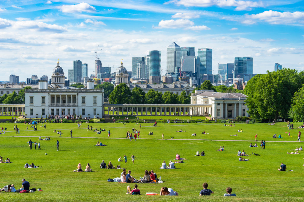 A shot of people lounging around in Greenwich Park on a sunny spring day, with London's high-rise buildings visible in the distance