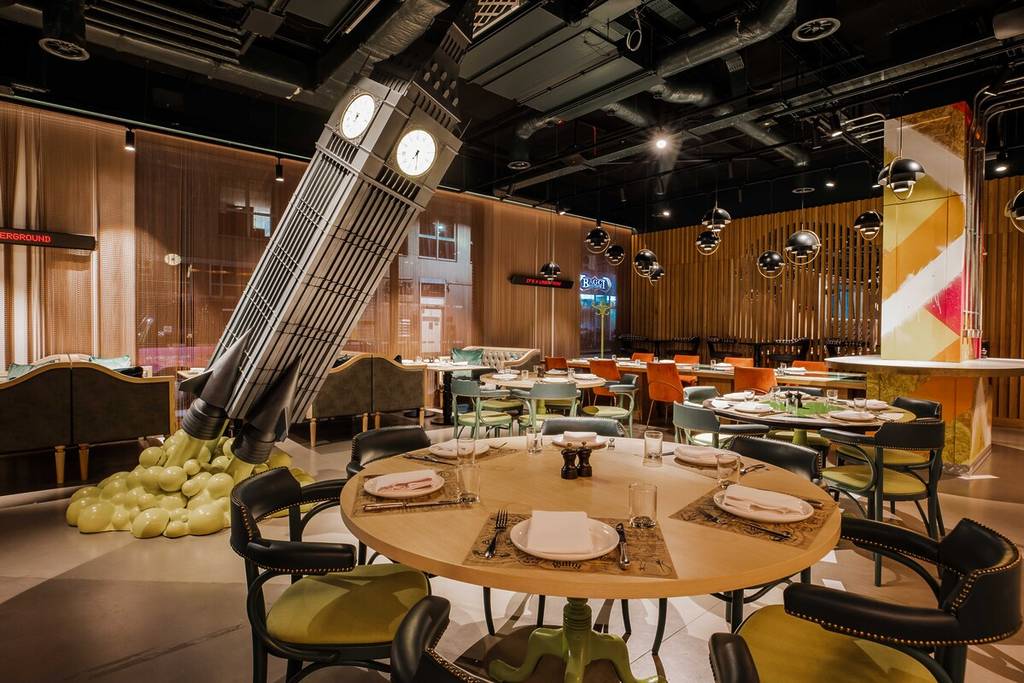 the eclectic interior of guilty by olivier, a new restaurant in London, showing a big ben model about to take off like a rocket amidst dining tables