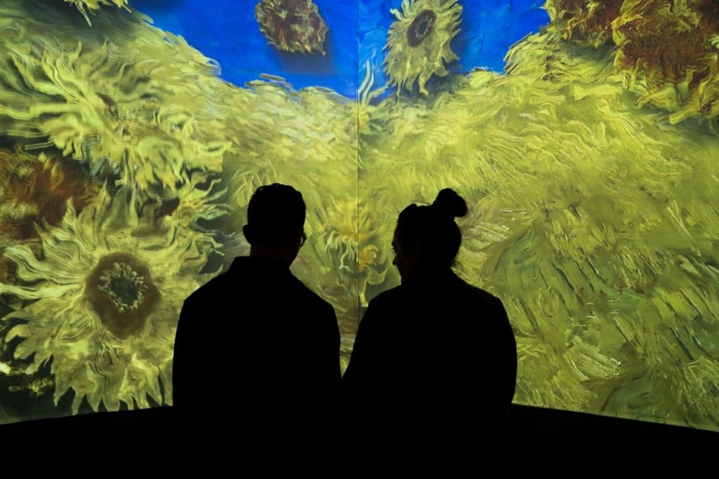 Two people watch the sunflowers bloom at London's immersive Van Gogh exhibition.
