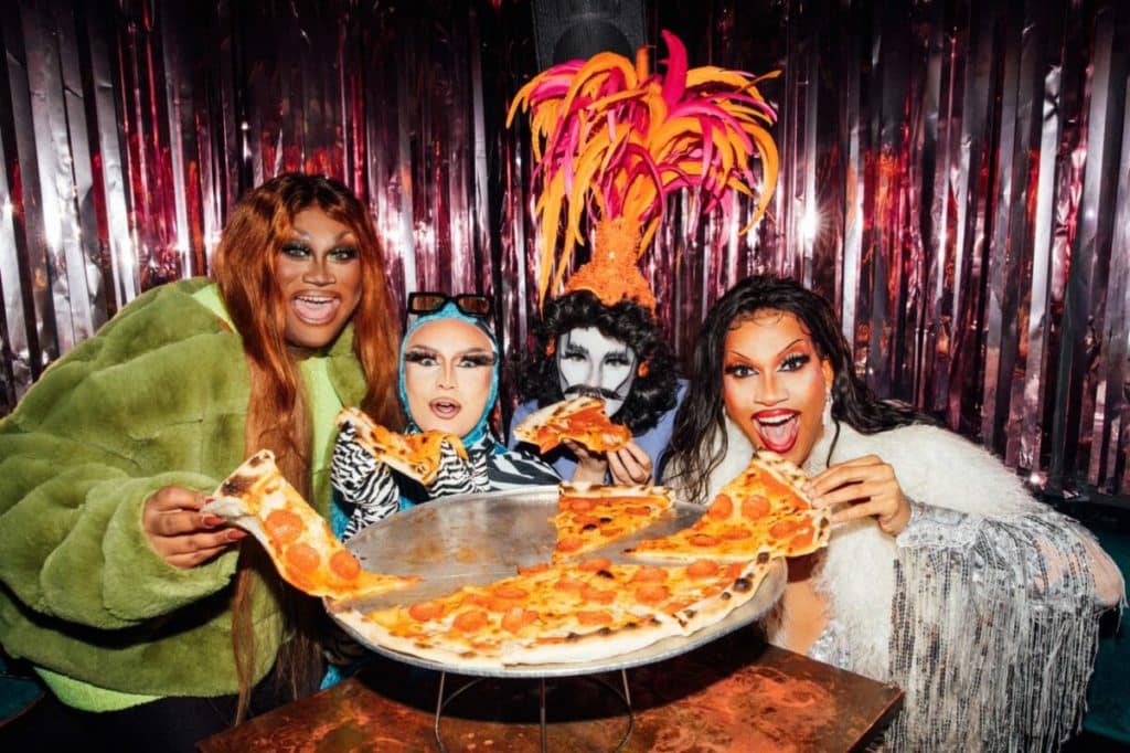 four drag performers holding slices of voodoo rays pizza with looks of amazement and joy on their faces