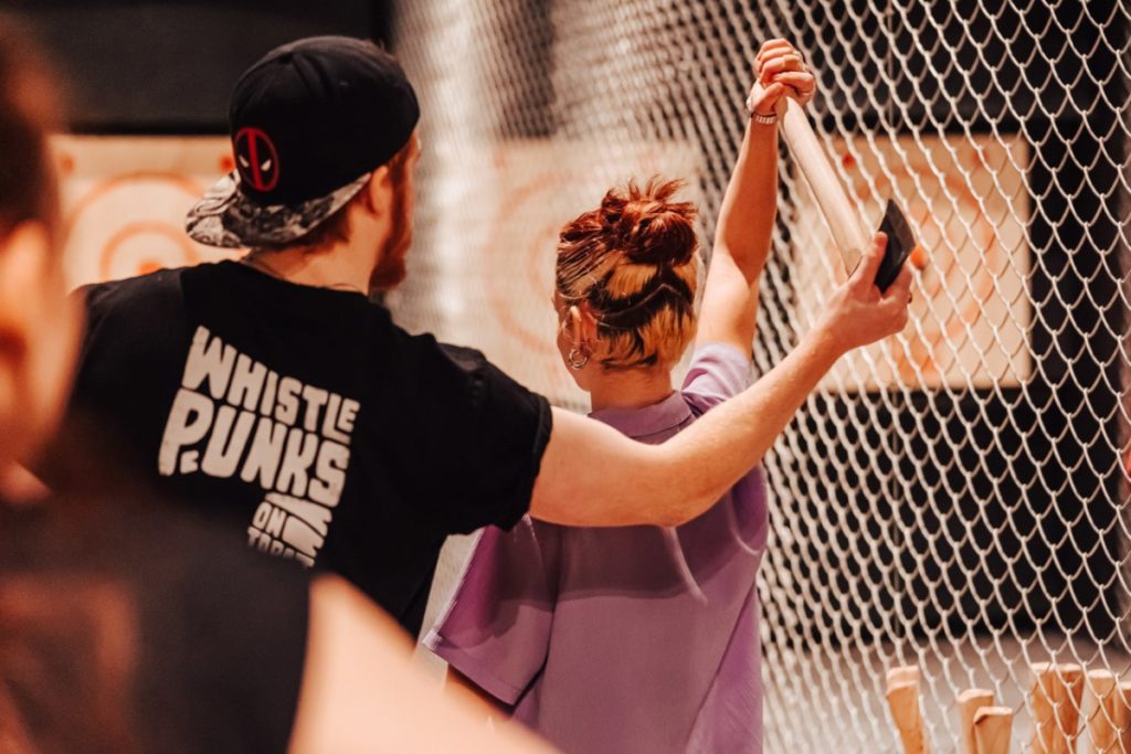 A woman about to throw an axe with a coach guiding her at Whistle Punks, one of the best places for axe throwing in London
