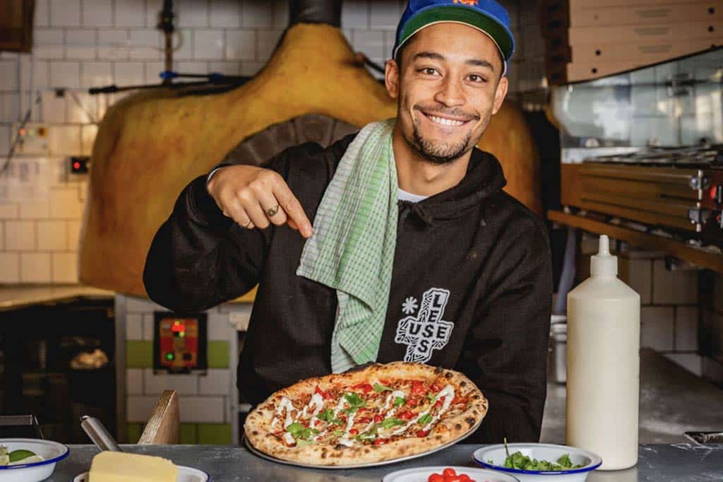 someone smiling and pointing at a pizza in their hand